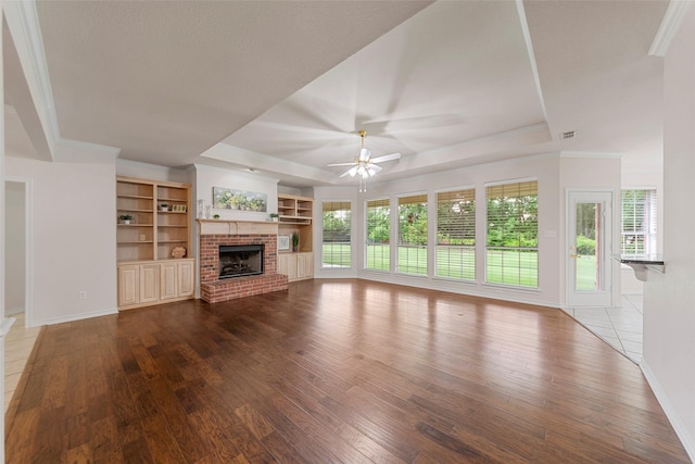 2403 Berry Grove Ct, Melissa, TX 75454 - unfurnished living room featuring a tray ceiling, a brick fireplace, hardwood / wood-style flooring, crown molding, and a ceiling fan