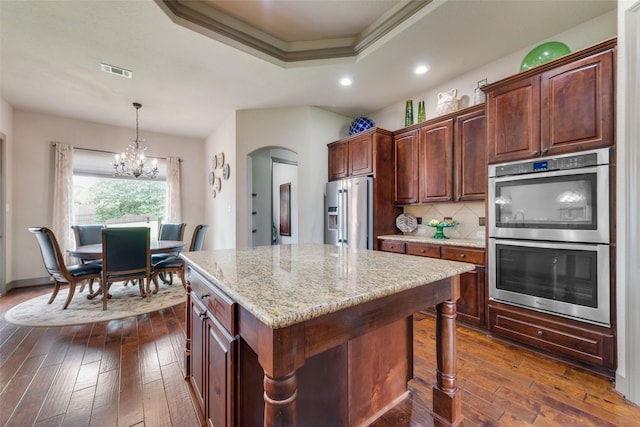 206 Hidden Meadow Cir, Midlothian, TX 76065 - kitchen with stainless steel appliances, a raised ceiling, dark wood finished floors, arched walkways, and a chandelier