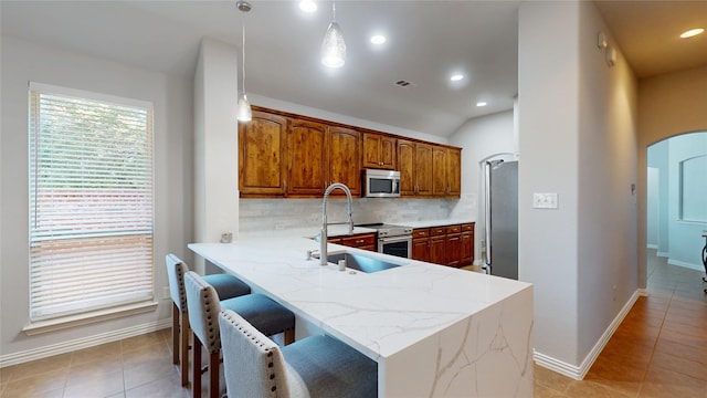 751 Kirby Dr, Argyle, TX 76226 - kitchen featuring appliances with stainless steel finishes, arched walkways, backsplash, light tile patterned floors, and brown cabinets