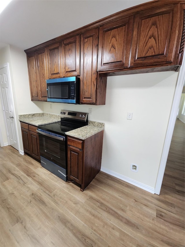 1721 Monaco Dr, Arlington, TX 76010 - kitchen featuring stainless steel microwave, range with electric stovetop, light wood-style flooring, light stone countertops, and dark brown cabinets