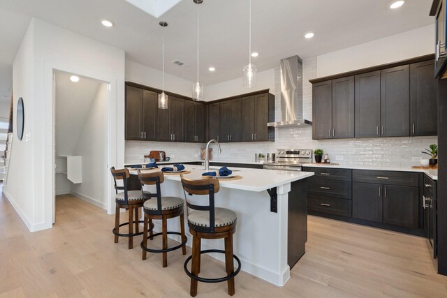 2105 Oak Haven Ct, Garland, TX 75044 - kitchen featuring wall chimney exhaust hood, stainless steel range with electric cooktop, a breakfast bar area, light countertops, and light wood-style floors