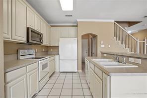 5729 Blackmon Ct, Fort Worth, TX 76137 - kitchen featuring white appliances, arched walkways, light tile patterned floors, a center island with sink, and light countertops