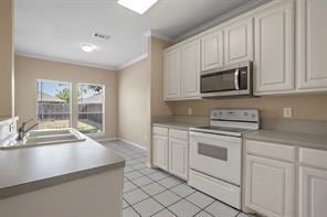 5729 Blackmon Ct, Fort Worth, TX 76137 - kitchen with stainless steel microwave, white range with electric cooktop, crown molding, white cabinetry, and light tile patterned floors