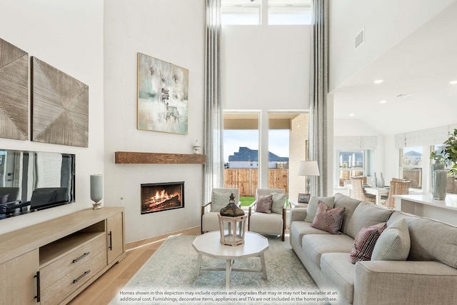 3803 Hidden Cove Ct, Rockwall, TX 75032 - living area featuring a high ceiling, light wood-type flooring, healthy amount of natural light, and a warm lit fireplace