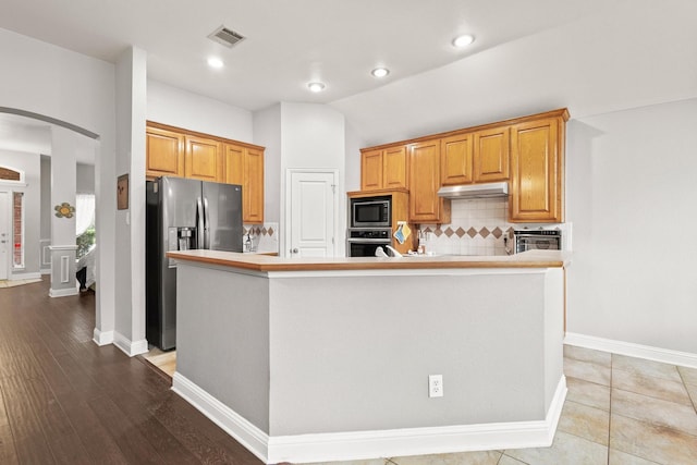 2009 Lake Fork Ct, Denton, TX 76210 - kitchen featuring appliances with stainless steel finishes, arched walkways, under cabinet range hood, tasteful backsplash, and light countertops
