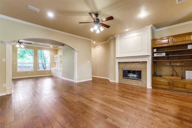 3506 Ash Cir, Richardson, TX 75082 - unfurnished living room with a ceiling fan, arched walkways, light wood-style floors, a fireplace, and crown molding