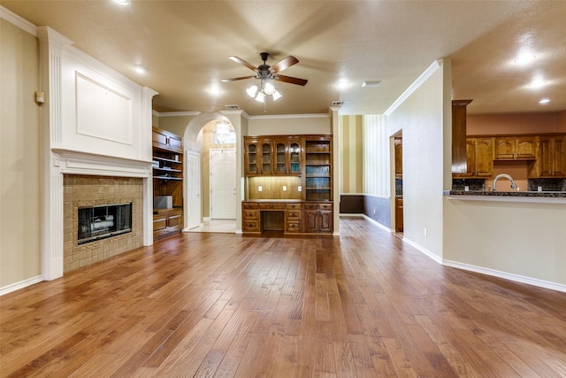 3506 Ash Cir, Richardson, TX 75082 - unfurnished living room featuring a ceiling fan, ornamental molding, hardwood / wood-style flooring, a tile fireplace, and arched walkways