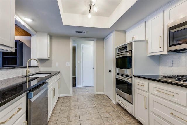1902 Vassar Dr, Richardson, TX 75081 - kitchen featuring appliances with stainless steel finishes, a tray ceiling, white cabinets, tasteful backsplash, and dark stone counters