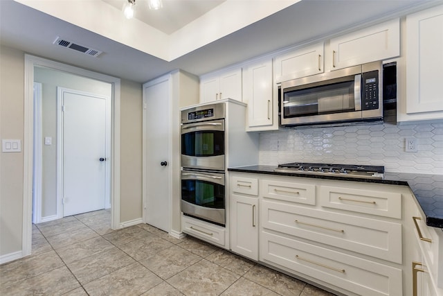 1902 Vassar Dr, Richardson, TX 75081 - kitchen featuring appliances with stainless steel finishes, backsplash, white cabinetry, light tile patterned floors, and dark stone counters