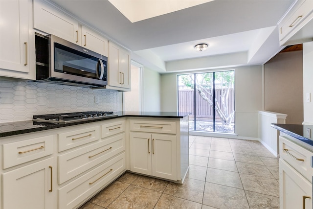 1902 Vassar Dr, Richardson, TX 75081 - kitchen with appliances with stainless steel finishes, decorative backsplash, white cabinets, dark stone counters, and light tile patterned flooring