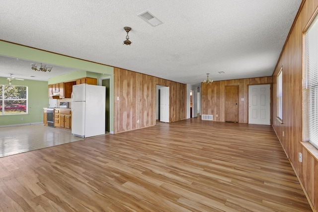 1210 E Fm 902, Howe, TX 75459 - unfurnished living room with a chandelier, wood walls, light wood-style floors, and a textured ceiling
