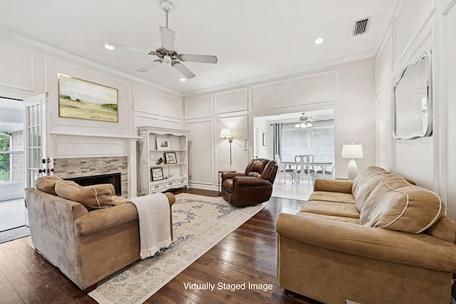 312 Bluffview Ct, Forney, TX 75126 - living room with a decorative wall, ornamental molding, a ceiling fan, a stone fireplace, and dark wood-type flooring