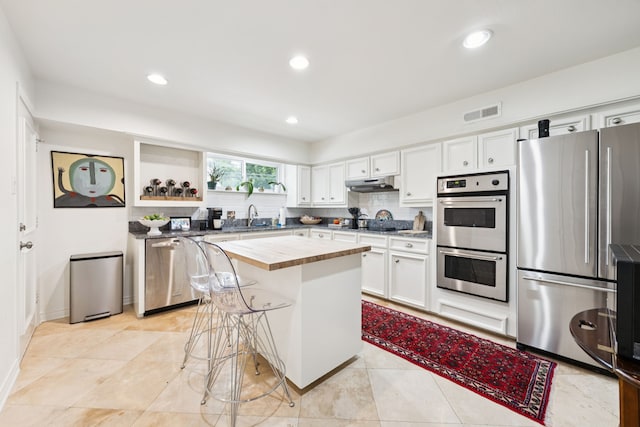 6227 Bandera Ave Unit D, Dallas, TX 75225 - kitchen featuring appliances with stainless steel finishes, white cabinets, decorative backsplash, butcher block countertops, and a breakfast bar area