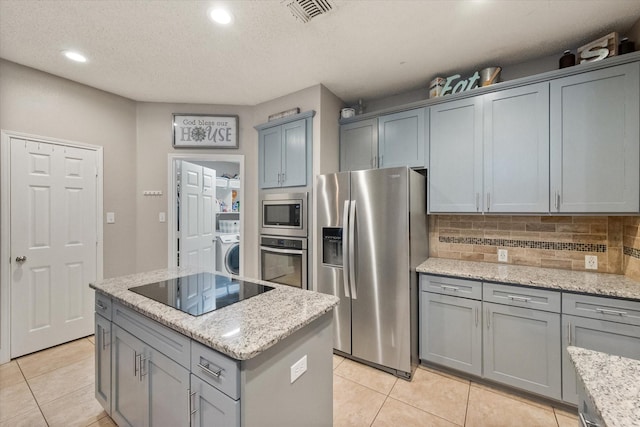 2213 Laura Elizabeth Trl, Mansfield, TX 76063 - kitchen with appliances with stainless steel finishes, washer / dryer, gray cabinetry, light tile patterned floors, and a kitchen island