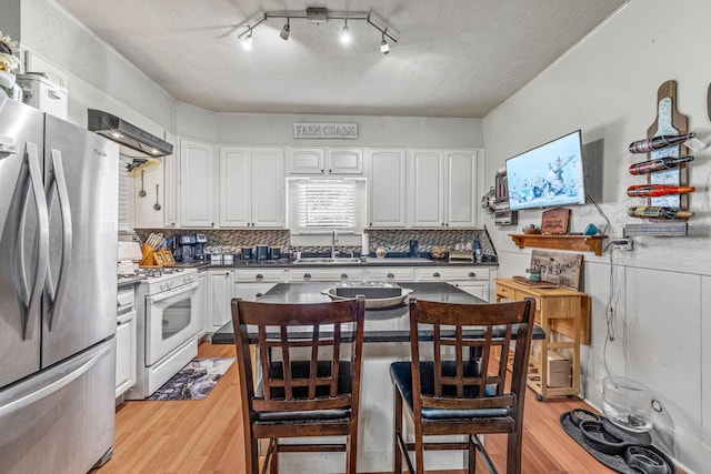 509 W Reynosa Ave, De Leon, TX 76444 - kitchen with freestanding refrigerator, white range with gas cooktop, light wood-type flooring, white cabinets, and a textured ceiling