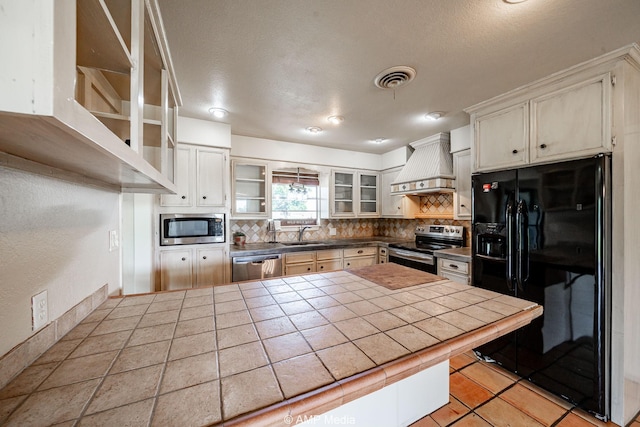 2306 County Road 475, Anson, TX 79501 - kitchen featuring appliances with stainless steel finishes, custom range hood, tile counters, backsplash, and a peninsula