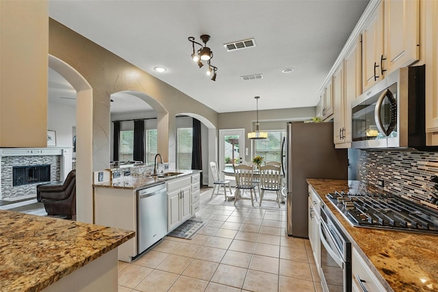 1330 Scarboro Hills Ln, Rockwall, TX 75087 - kitchen featuring appliances with stainless steel finishes, decorative backsplash, a tile fireplace, light tile patterned floors, and pendant lighting