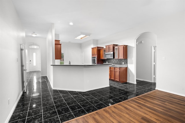 908 Trinity Dr, Lancaster, TX 75146 - kitchen with appliances with stainless steel finishes, backsplash, a peninsula, brown cabinetry, and dark tile patterned floors