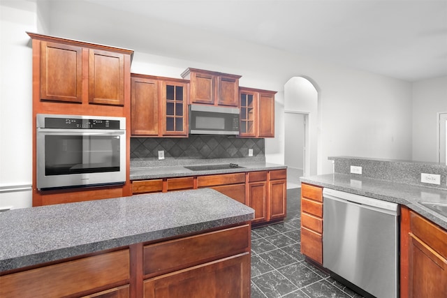 908 Trinity Dr, Lancaster, TX 75146 - kitchen featuring stainless steel appliances, backsplash, arched walkways, glass insert cabinets, and dark countertops