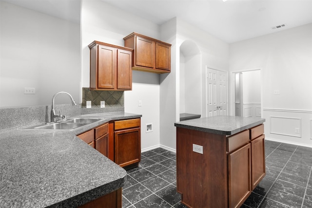 908 Trinity Dr, Lancaster, TX 75146 - kitchen with a center island, backsplash, dark countertops, arched walkways, and brown cabinets