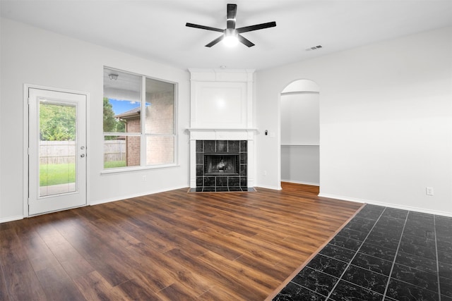 908 Trinity Dr, Lancaster, TX 75146 - unfurnished living room with a ceiling fan, arched walkways, a tiled fireplace, and dark wood-type flooring