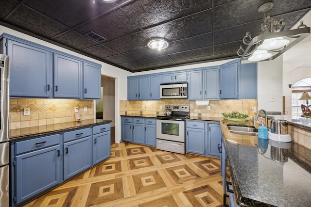 1701 Prairie Creek Ct, Garland, TX 75040 - kitchen featuring blue cabinets, stainless steel appliances, decorative backsplash, and dark stone counters