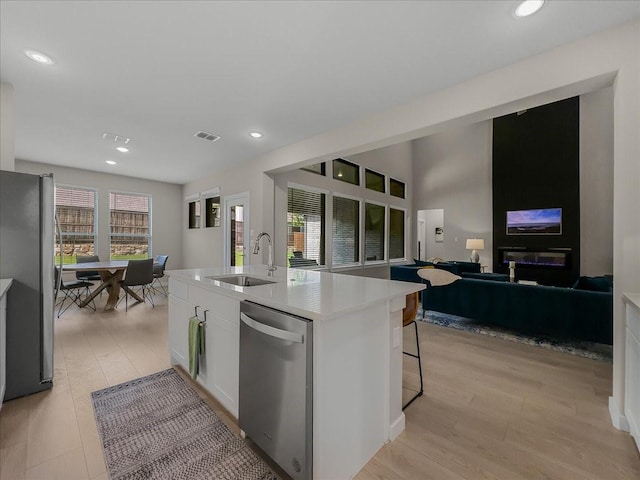 413 Coyote Creek Dr, Lavon, TX 75166 - kitchen featuring appliances with stainless steel finishes, light wood finished floors, white cabinets, an island with sink, and light countertops