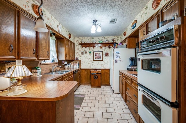 12869 Fm 1385, Pilot Point, TX 76258 - kitchen with wallpapered walls, a peninsula, dishwasher, brown cabinets, and a textured ceiling
