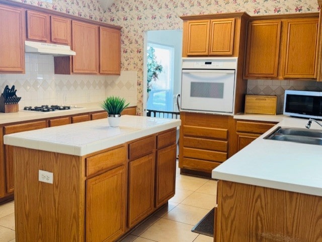 2322 Greenfield Cir, Garland, TX 75040 - kitchen featuring white appliances, wallpapered walls, under cabinet range hood, tasteful backsplash, and a kitchen island