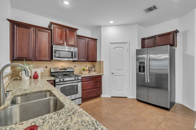 9700 Mulligan Dr, Mckinney, TX 75072 - kitchen featuring stainless steel appliances, tasteful backsplash, light stone countertops, light tile patterned flooring, and reddish brown cabinets