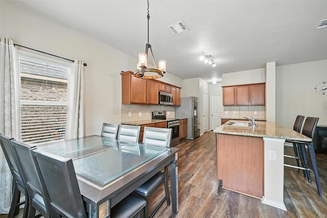 1209 Jasper Xing, Princeton, TX 75407 - kitchen with appliances with stainless steel finishes, dark wood-type flooring, tasteful backsplash, brown cabinets, and a breakfast bar