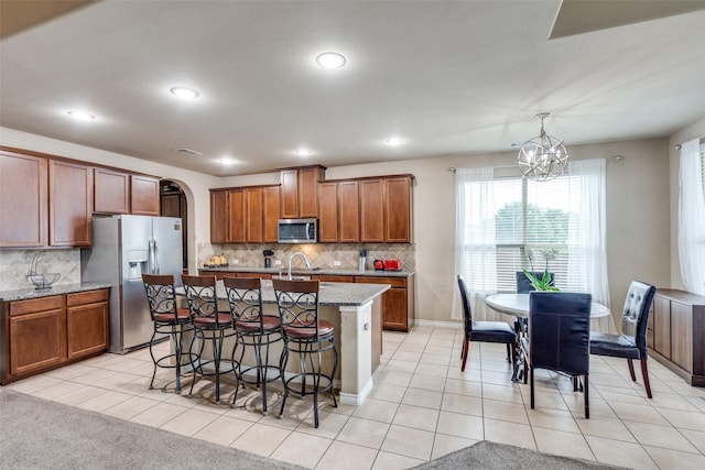 3820 Buchanan St, Mckinney, TX 75071 - kitchen with stainless steel appliances, a kitchen bar, brown cabinetry, arched walkways, and recessed lighting