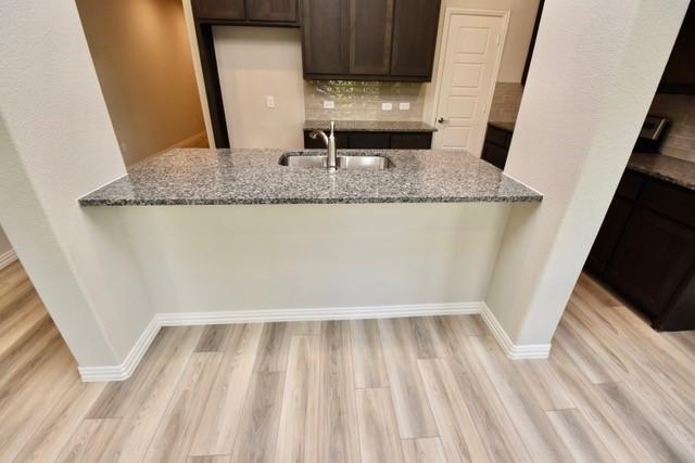 2609 Donella Dr, Denton, TX 76207 - kitchen featuring a peninsula, stone countertops, dark brown cabinetry, and light wood finished floors