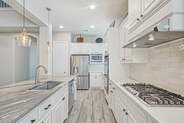 1701 Trinidad Way, Argyle, TX 76226 - kitchen featuring appliances with stainless steel finishes, ventilation hood, white cabinetry, tasteful backsplash, and light stone countertops