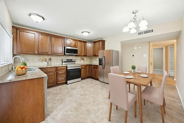 5109 Bartlett Dr, The Colony, TX 75056 - kitchen with appliances with stainless steel finishes, decorative backsplash, a chandelier, brown cabinets, and decorative light fixtures