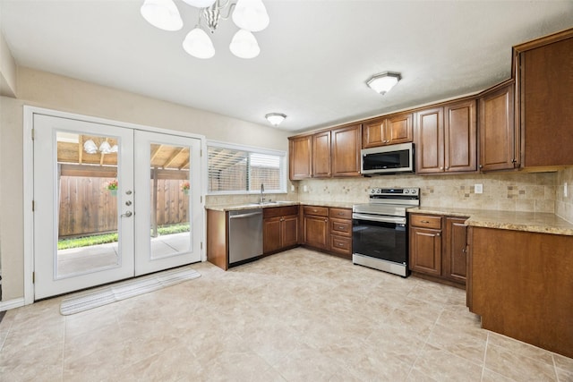 5109 Bartlett Dr, The Colony, TX 75056 - kitchen featuring stainless steel appliances, french doors, backsplash, a chandelier, and brown cabinetry