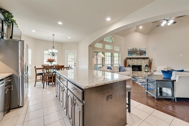 1220 Glendon Dr, Forney, TX 75126 - kitchen featuring appliances with stainless steel finishes, a stone fireplace, a kitchen bar, arched walkways, and a kitchen island