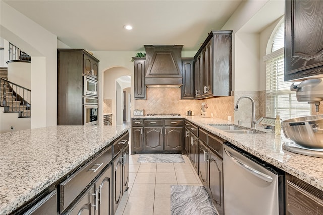 1220 Glendon Dr, Forney, TX 75126 - kitchen with appliances with stainless steel finishes, premium range hood, arched walkways, dark brown cabinets, and tasteful backsplash