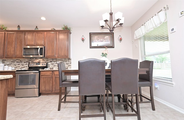 3209 Silver Point Ct, Mansfield, TX 76063 - kitchen with appliances with stainless steel finishes, a chandelier, tasteful backsplash, brown cabinets, and light tile patterned flooring