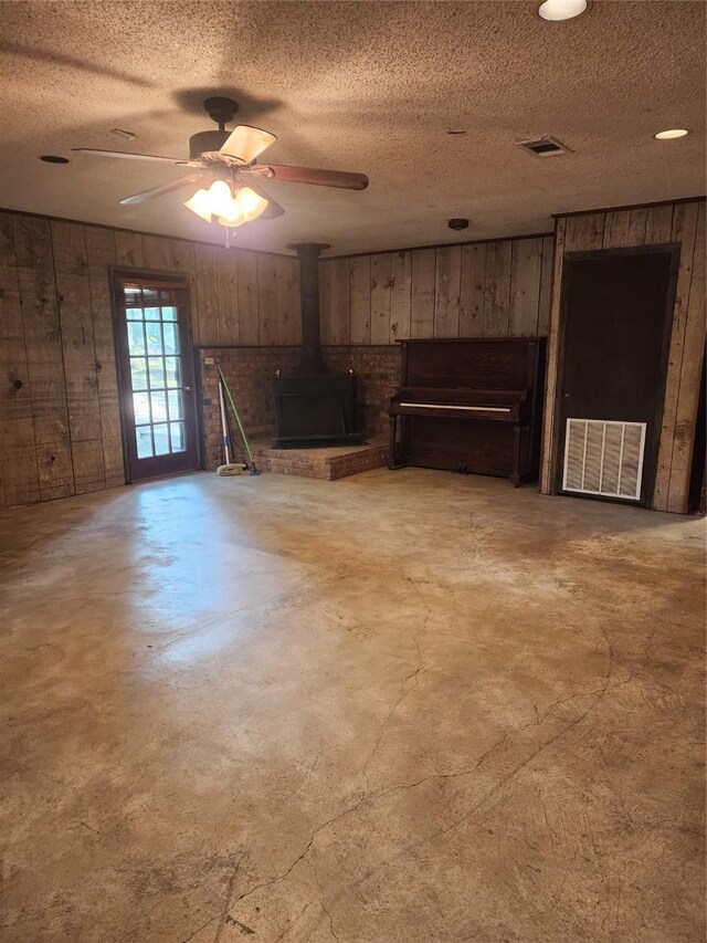 34 Sunset Blvd, Star Harbor, TX 75148 - unfurnished living room with wooden walls, concrete floors, a wood stove, a textured ceiling, and ceiling fan