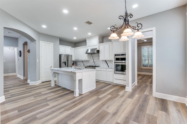 11722 Estacado Dr, Frisco, TX 75033 - kitchen featuring appliances with stainless steel finishes, extractor fan, arched walkways, white cabinetry, and tasteful backsplash