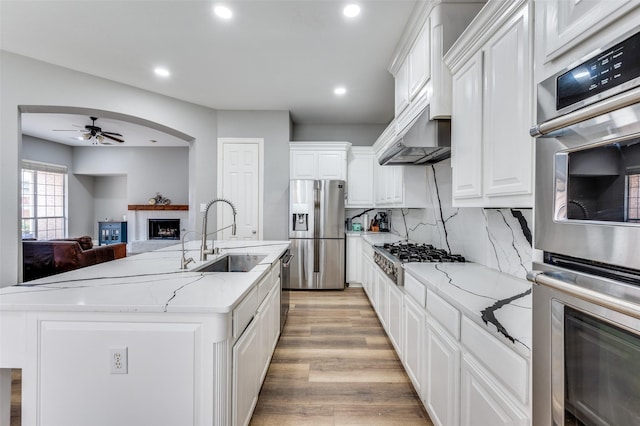 11722 Estacado Dr, Frisco, TX 75033 - kitchen featuring stainless steel appliances, a ceiling fan, a fireplace, light wood-style floors, and white cabinetry