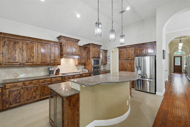2428 Lilyfield Dr, Trophy Club, TX 76262 - kitchen with appliances with stainless steel finishes, arched walkways, dark stone countertops, an island with sink, and hanging light fixtures
