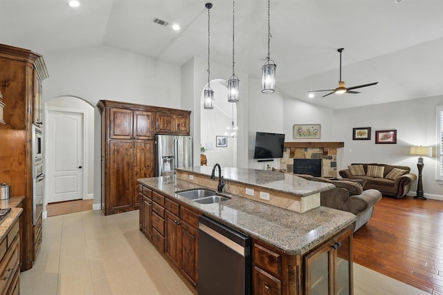 2428 Lilyfield Dr, Trophy Club, TX 76262 - kitchen with appliances with stainless steel finishes, ceiling fan, a center island with sink, a fireplace, and light stone countertops