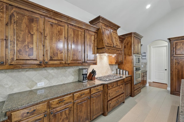 2428 Lilyfield Dr, Trophy Club, TX 76262 - kitchen with appliances with stainless steel finishes, decorative backsplash, dark stone counters, lofted ceiling, and arched walkways
