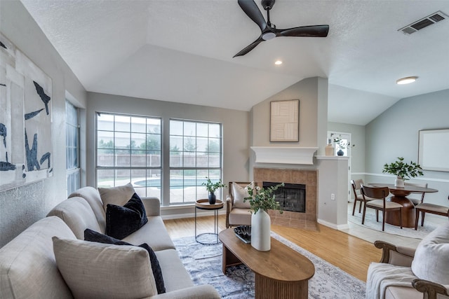 10715 Robincreek Ln, Frisco, TX 75035 - living room with a ceiling fan, vaulted ceiling, wood finished floors, a fireplace, and a textured ceiling