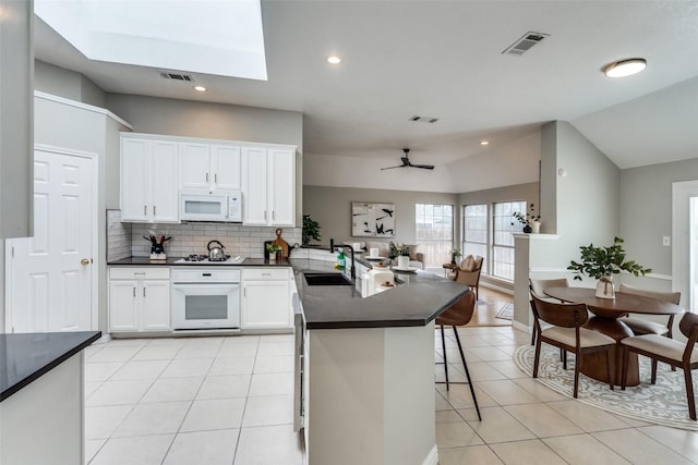 10715 Robincreek Ln, Frisco, TX 75035 - kitchen with white appliances, dark countertops, light tile patterned flooring, a peninsula, and lofted ceiling