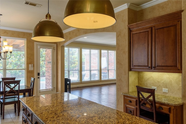 11819 Coronado Trl, Frisco, TX 75033 - kitchen featuring arched walkways, dark stone countertops, brown cabinets, decorative light fixtures, and crown molding
