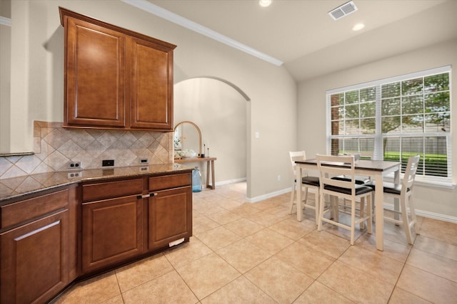 1224 Shelley Dr, Burleson, TX 76028 - kitchen featuring crown molding, arched walkways, tasteful backsplash, light tile patterned floors, and dark stone counters