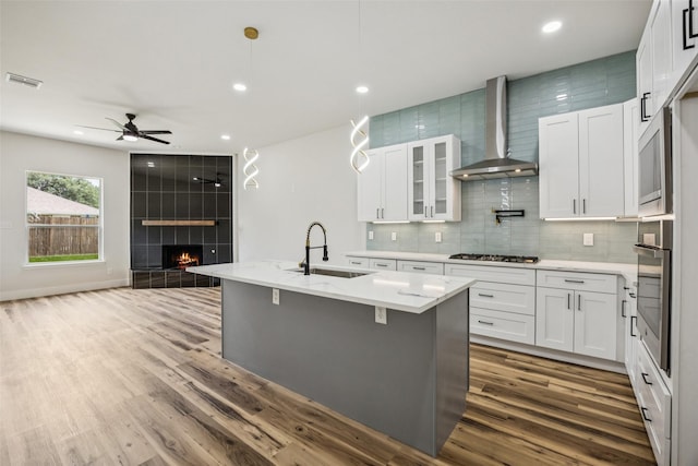 15578 Wrangler Dr, Frisco, TX 75035 - kitchen with wall chimney exhaust hood, a tiled fireplace, wood finished floors, a ceiling fan, and decorative backsplash